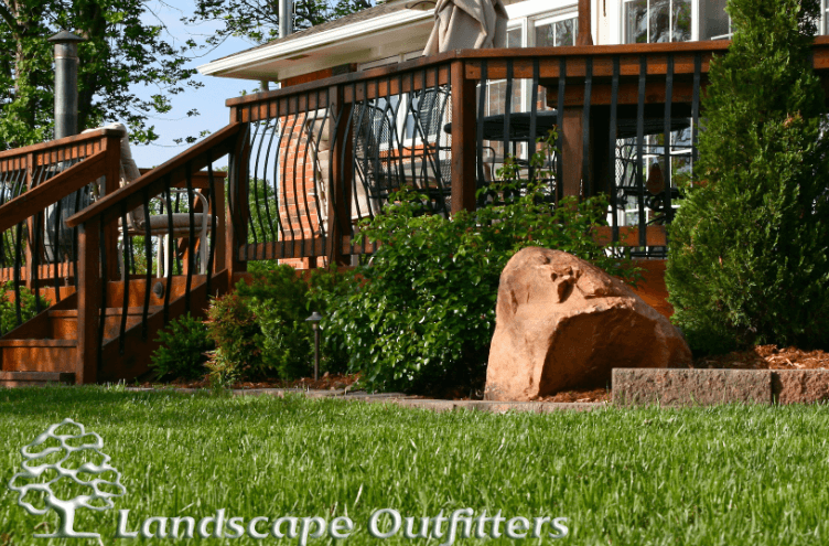 View of wooden patio with a green lawn, shrubs, and stone in the foreground