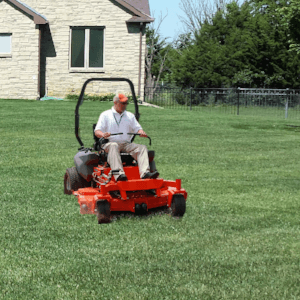 Man mowing a green lawn in front of a stone home